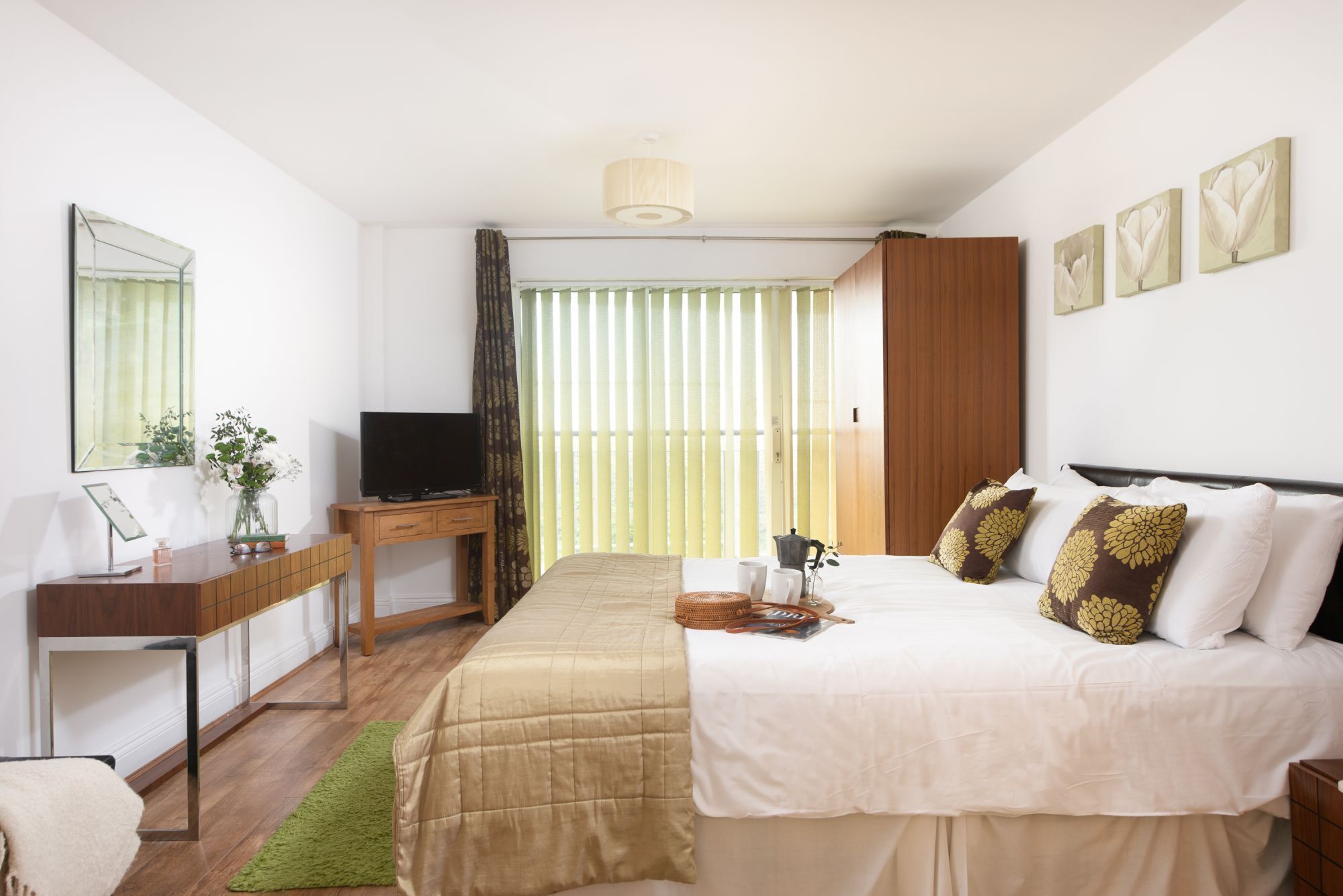 Habitación de hotel con cama, escritorio con televisor, espejo y ventana con persianas.