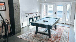 A pool table in a room with a patterned rug, a ceiling light fixture, and a door leading outside.