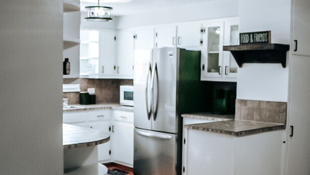 A modern kitchen with white cabinets, stainless steel appliances, and a wooden floor.