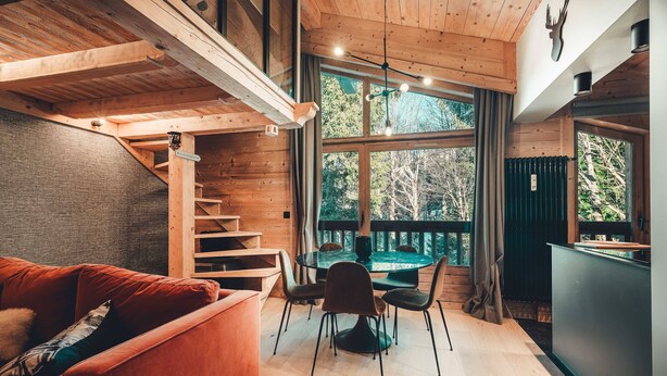 Ein Holzinterieur mit einer Treppe, einem Essbereich mit Stühlen, einem Tisch und einer Couch.