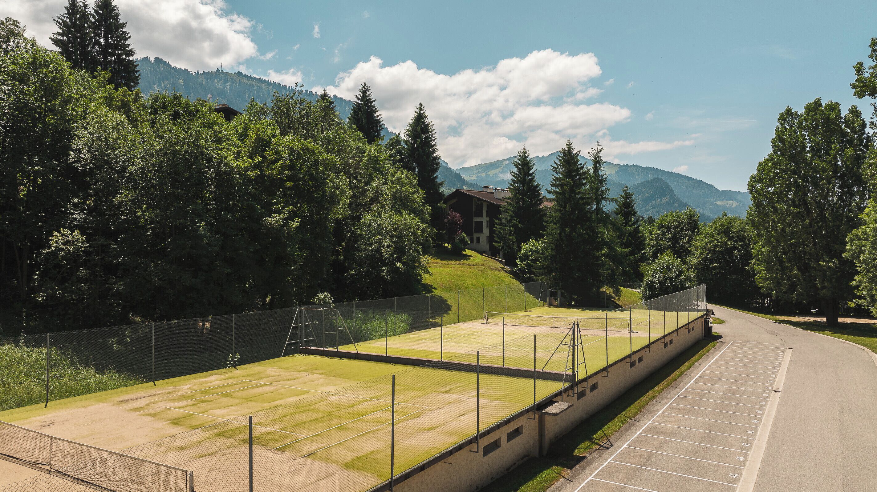 A tennis court with a net, surrounded by trees and a building in the background.