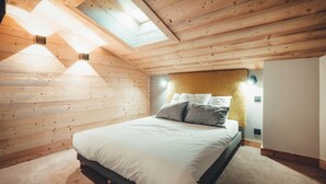 Ein Schlafzimmer mit Holzbalkendecke, einem Bett mit weißer Bettwäsche und zwei Wandleuchten.