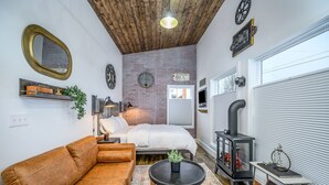 Una habitación acogedora con una cama, un sofá, una mesita, una chimenea y una pared de ladrillo.