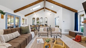 A spacious living room with a high ceiling, exposed wooden beams, a brown sofa, a coffee table, and a dining area in the background. - Free Heated Pool ~ Hot Tub ~ Basement Game Room ~ Large Backyard (Mesa)