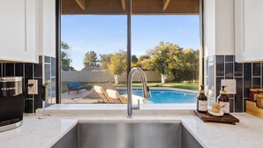 A kitchen with a large window overlooking a backyard with a pool and outdoor furniture. - Free Heated Pool ~ Hot Tub ~ Basement Game Room ~ Large Backyard (Mesa)