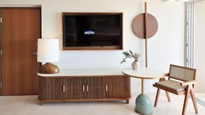 Una sala de estar moderna con televisor, un mueble de madera, una mesa redonda, una silla y una lámpara.