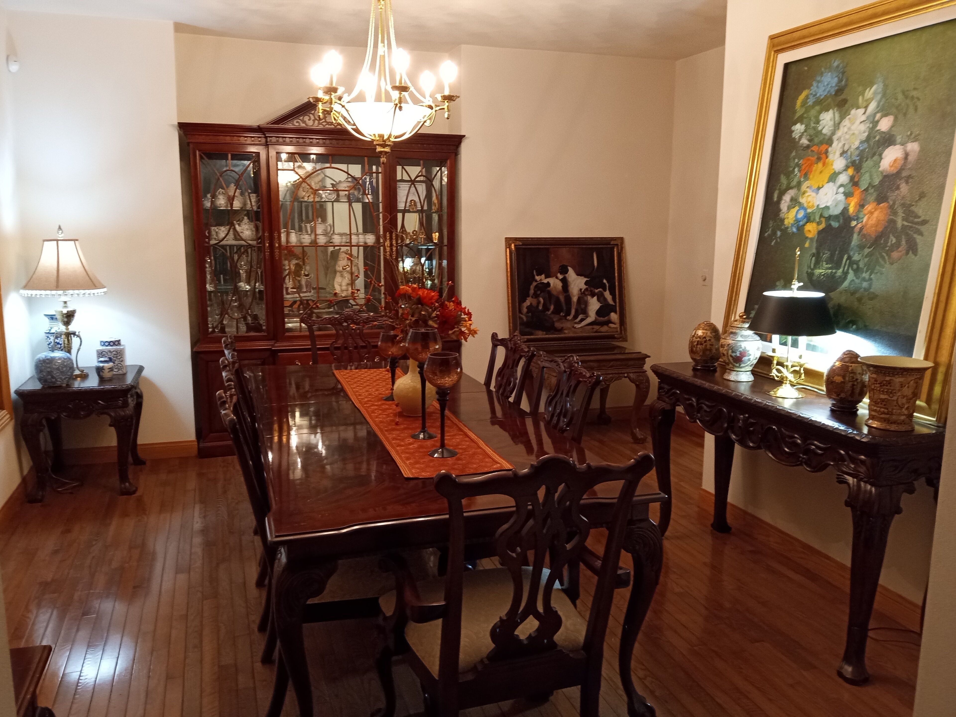 Ein Esszimmer mit Holztisch, Stühlen, einer Chandelierleuchtre und einem Gemälde.