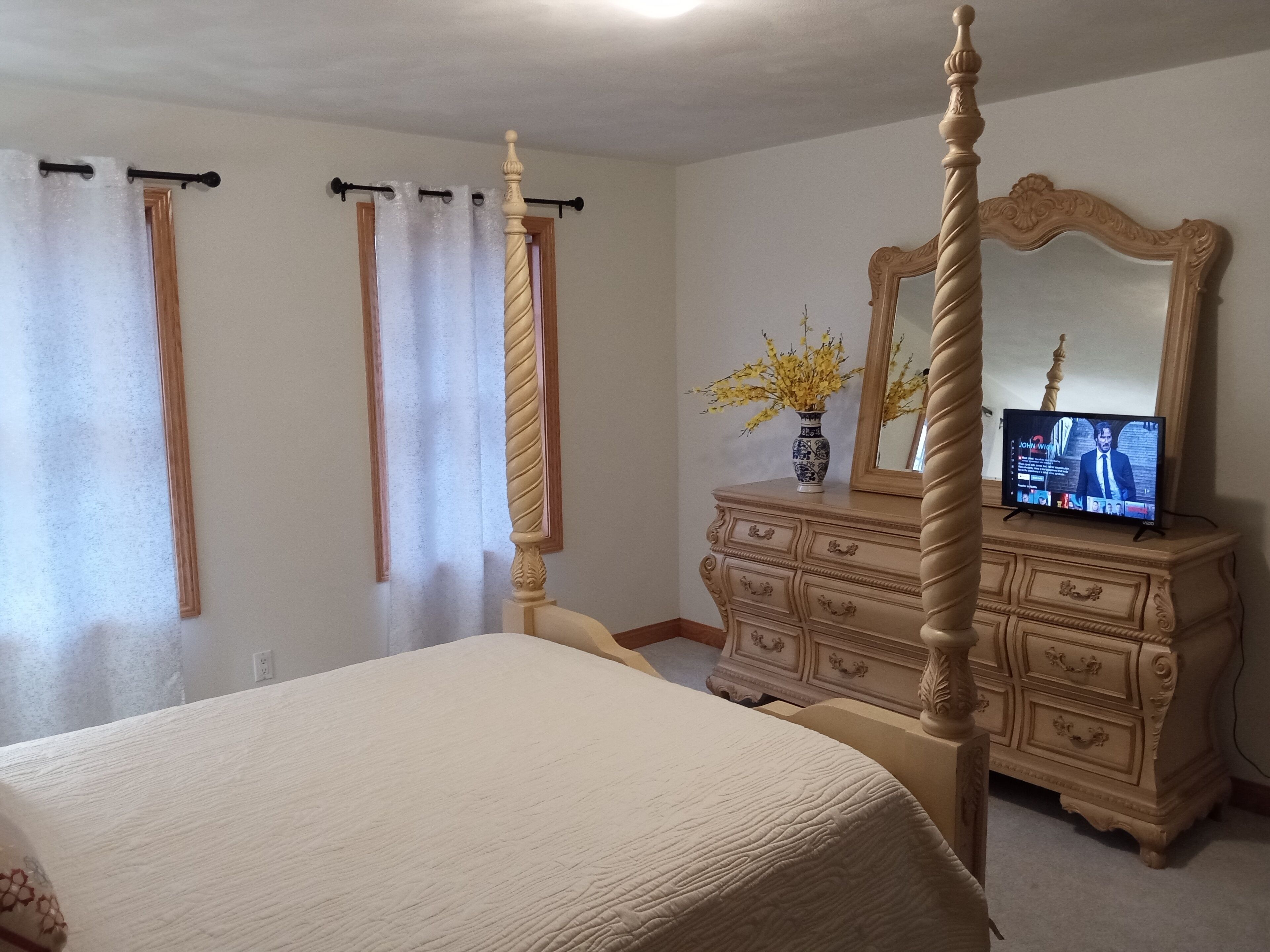 A bedroom with a four-poster bed, a dresser with a mirror, and a television on the dresser.