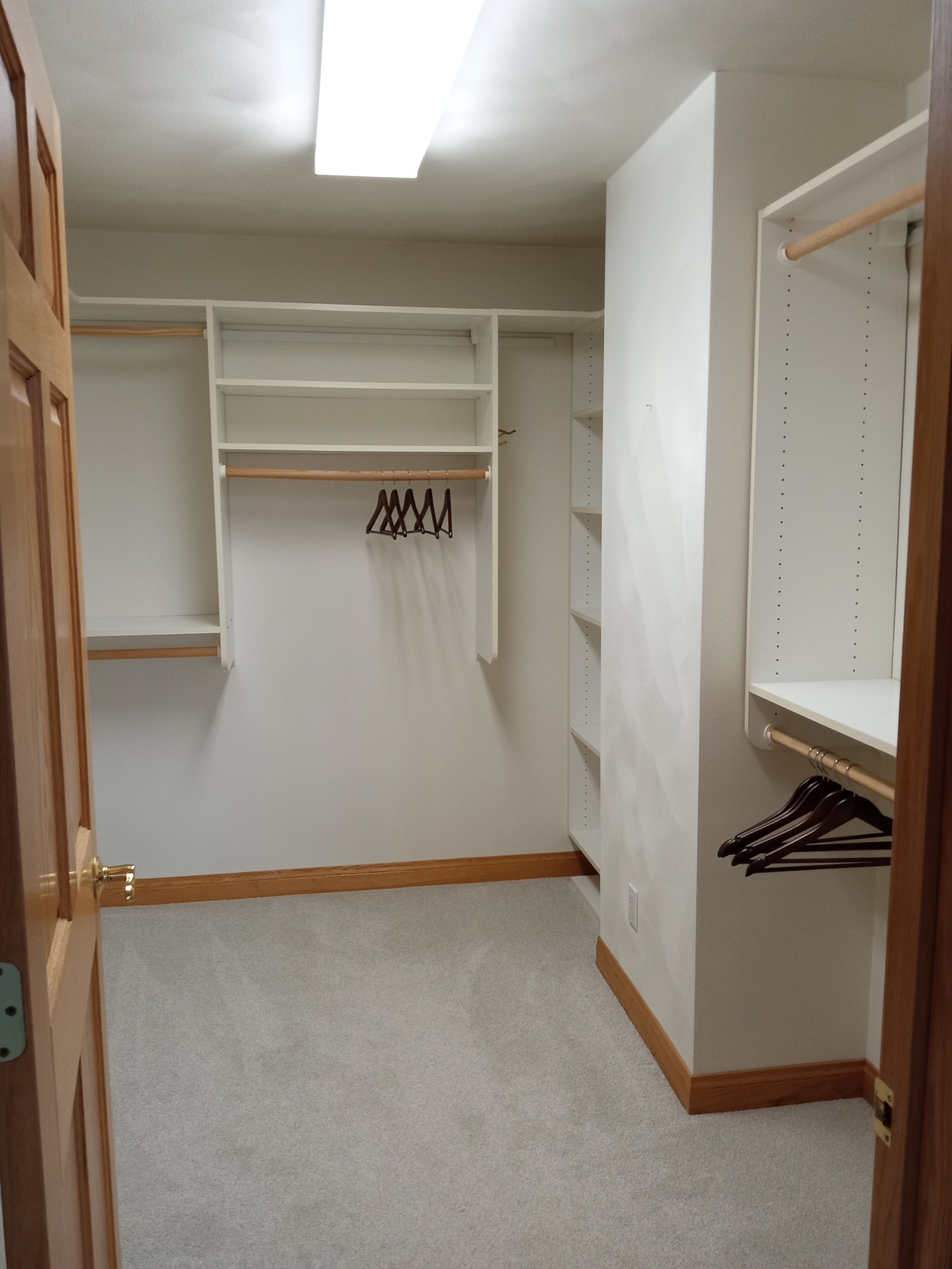 A walk-in closet with open shelves, a wooden floor, and a ceiling light.