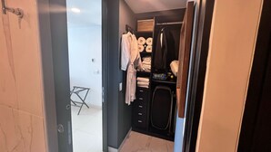 Un baño moderno con ducha a ras de suelo, inodoro y lavabo. Hay un perchero con toallas y un estante con artículos de aseo.