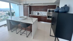 Una cocina moderna con una isla grande, armarios de madera oscura, electrodomésticos de acero inoxidable y vistas de la ciudad.