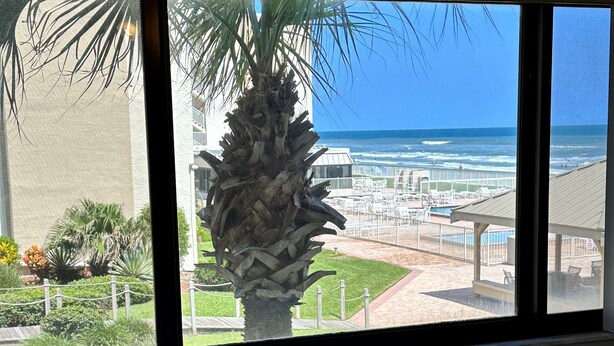 Ein Zimmer mit großem Fenster mit Blick auf Strand und Poolbereich.
