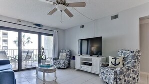 Ein Wohnzimmer mit Fernseher, zwei gemusterten Sesseln, einem Couchtisch und einem Deckenventilator.