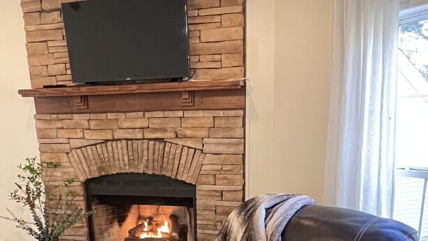 A leather recliner with a blanket, a stone fireplace with a TV above, and a small table. - A Nordic cozy farm house, great green area,  (Pageland)