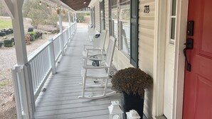 A covered porch with white rocking chairs and a potted plant. - A Nordic cozy farm house, great green area,  (Pageland)