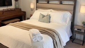 A neatly arranged hotel room with a large bed, a flat-screen TV, a wooden bench, and a small table with a lamp. - A Nordic cozy farm house, great green area,  (Pageland)