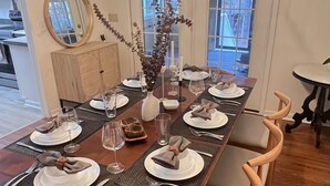 A dining room with a long wooden table set for six, surrounded by six wooden chairs. A large mirror hangs on the wall above the table, and a vase with dried branches is placed on the table. - A Nordic cozy farm house, great green area,  (Pageland)