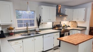 A modern kitchen with white cabinets, a stainless steel range hood, a double sink, and a wooden island. - A Nordic cozy farm house, great green area,  (Pageland)