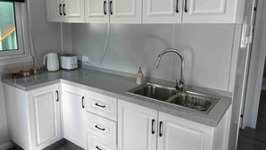 A kitchen with white cabinets, a stainless steel sink, and a countertop with a kettle and toaster. - Oliver’s Hut - Hartley Huts (Hartley Vale)