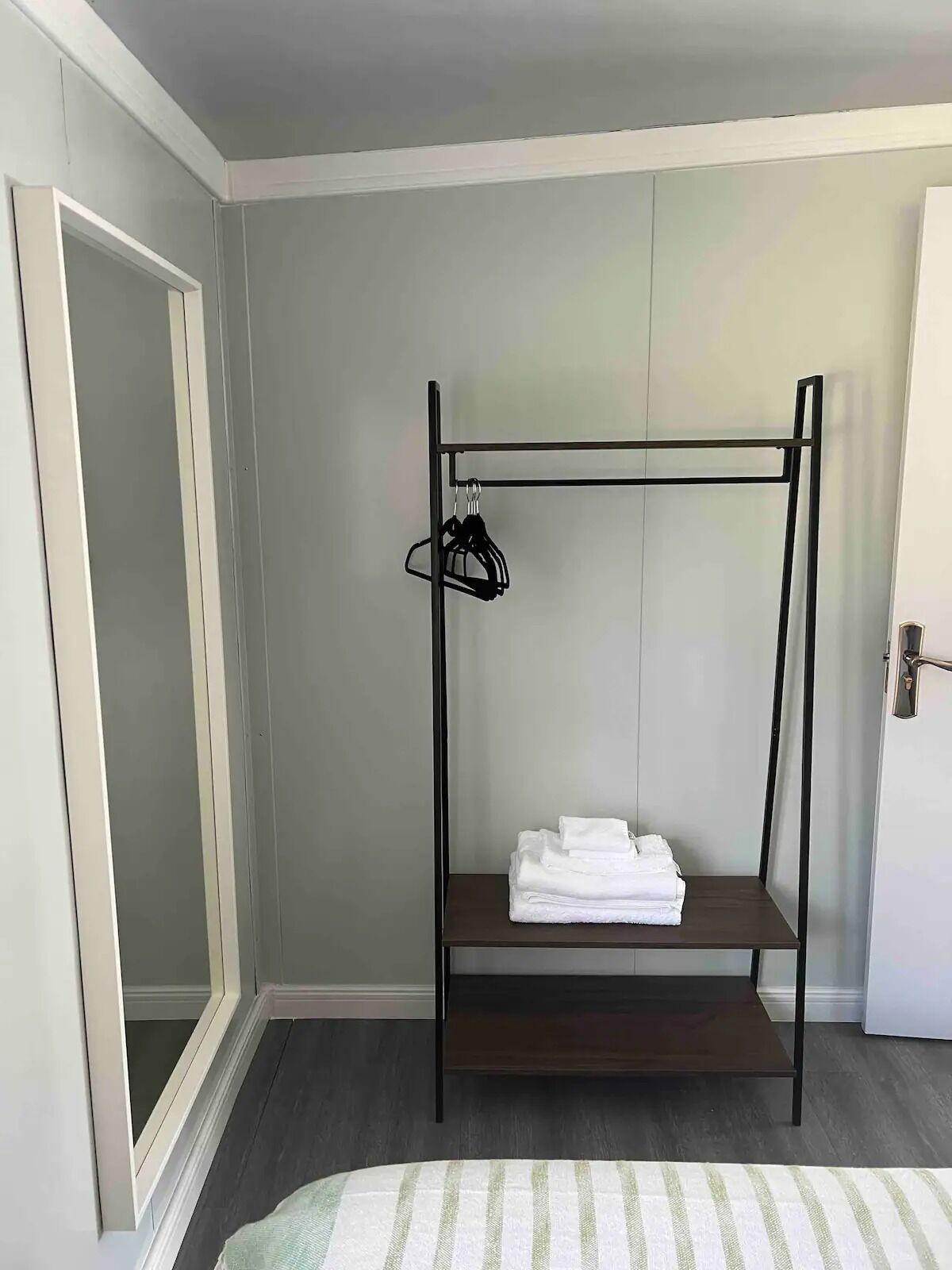 A room with a bunk bed, a small shelf with folded towels, a coat rack, and a door.