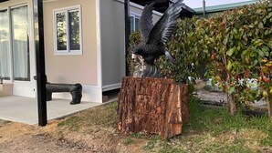 A modern building with a bench outside, a large bird sculpture, and a tree stump planter. - Yabba’s Hut - Hartley Huts (Hartley Vale)