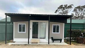 A small, single-story building with a covered porch, a bench, and a dog statue. - Yabba’s Hut - Hartley Huts (Hartley Vale)