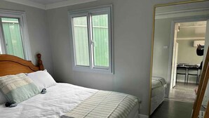A bedroom with a bed, a mirror, and a view of a dining area. - Yabba’s Hut - Hartley Huts (Hartley Vale)
