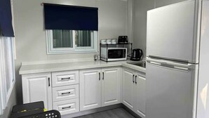 A compact kitchen with white cabinets, a microwave, a coffee maker, and a refrigerator. - Yabba’s Hut - Hartley Huts (Hartley Vale)