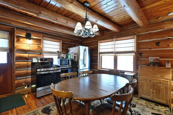 L’intérieur d’une cabane en rondins, avec une table à manger en bois, des chaises, un lustre, un réfrigérateur et un buffet en bois.