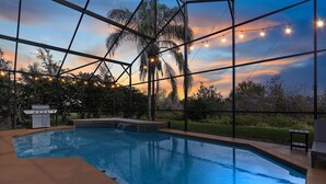 Una piscina interior con vistas a la puesta de sol a través de amplias ventanas, rodeada de una terraza con luces colgantes.