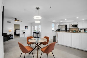 Een moderne keuken met witte kasten, roestvrijstalen apparatuur en een glazen eettafel met oranje stoelen.