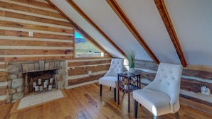 A log cabin interior with a stone fireplace, wooden beams, and a view of the outdoors. - Historical Paris Cabin on Farm w/ Fire Pit! (Paris)