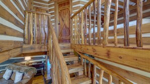 A wooden staircase with a rustic design, a leather sofa, and a wooden door. - Historical Paris Cabin on Farm w/ Fire Pit! (Paris)