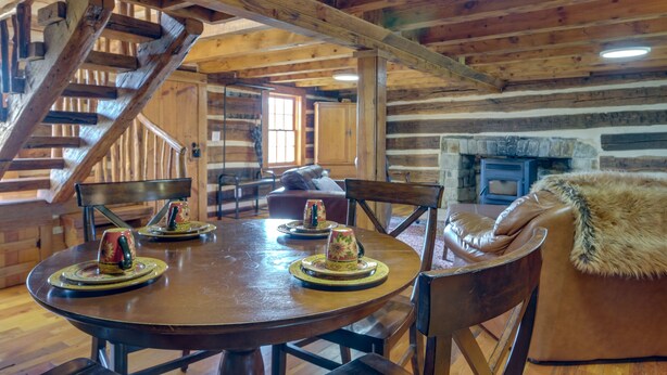 A wooden interior with a round dining table, chairs, a sofa, and a fireplace. - Historical Paris Cabin on Farm w/ Fire Pit! (Paris)