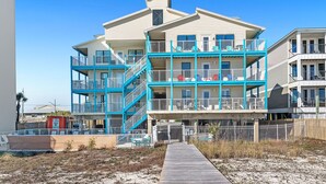 Un immeuble à plusieurs étages situé en bord de mer, doté de balcons, d’une promenade en bois et offrant un accès direct à la plage.