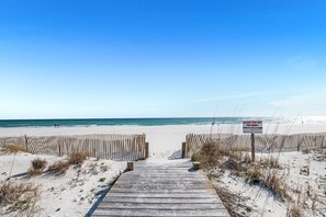 Una passerella in legno conduce a una spiaggia sabbiosa, con un cartello che avverte di non calpestare le dune.