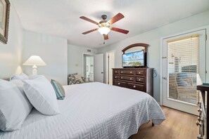 A bedroom with a bed, a ceiling fan, a dresser, a television, and a door with blinds.
