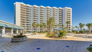 A hotel with a large, multi-story building, a paved courtyard with palm trees, and outdoor seating areas. - Palms of Destin Resort Condo: Beaches, Golf & More (Destin)