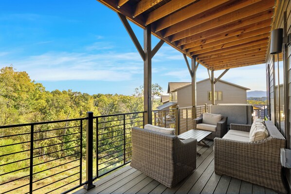 A covered outdoor seating area with wicker furniture and a view of a forested landscape.