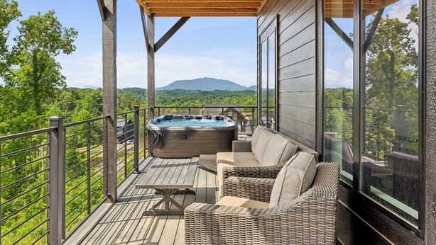 Una terraza de madera con un jacuzzi, muebles de mimbre y una vista panorámica de las montañas.