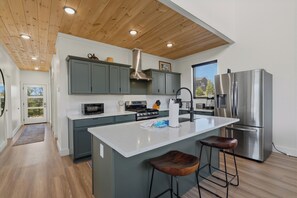 A modern kitchen with a large island, stainless steel appliances, and a wooden ceiling.
