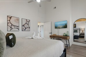 A hotel room with a bed, a desk, a mirror, and artwork on the walls. - Sleek 4BR Cabin with Hot Tub, Theater & Arcade | Golf & Waterpark Nearby! (Sevierville)