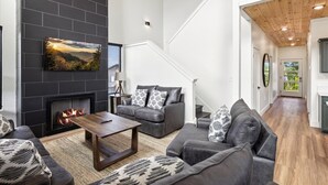 Una sala de estar moderna con chimenea, sofás grises y una escalera que sube a otro nivel.