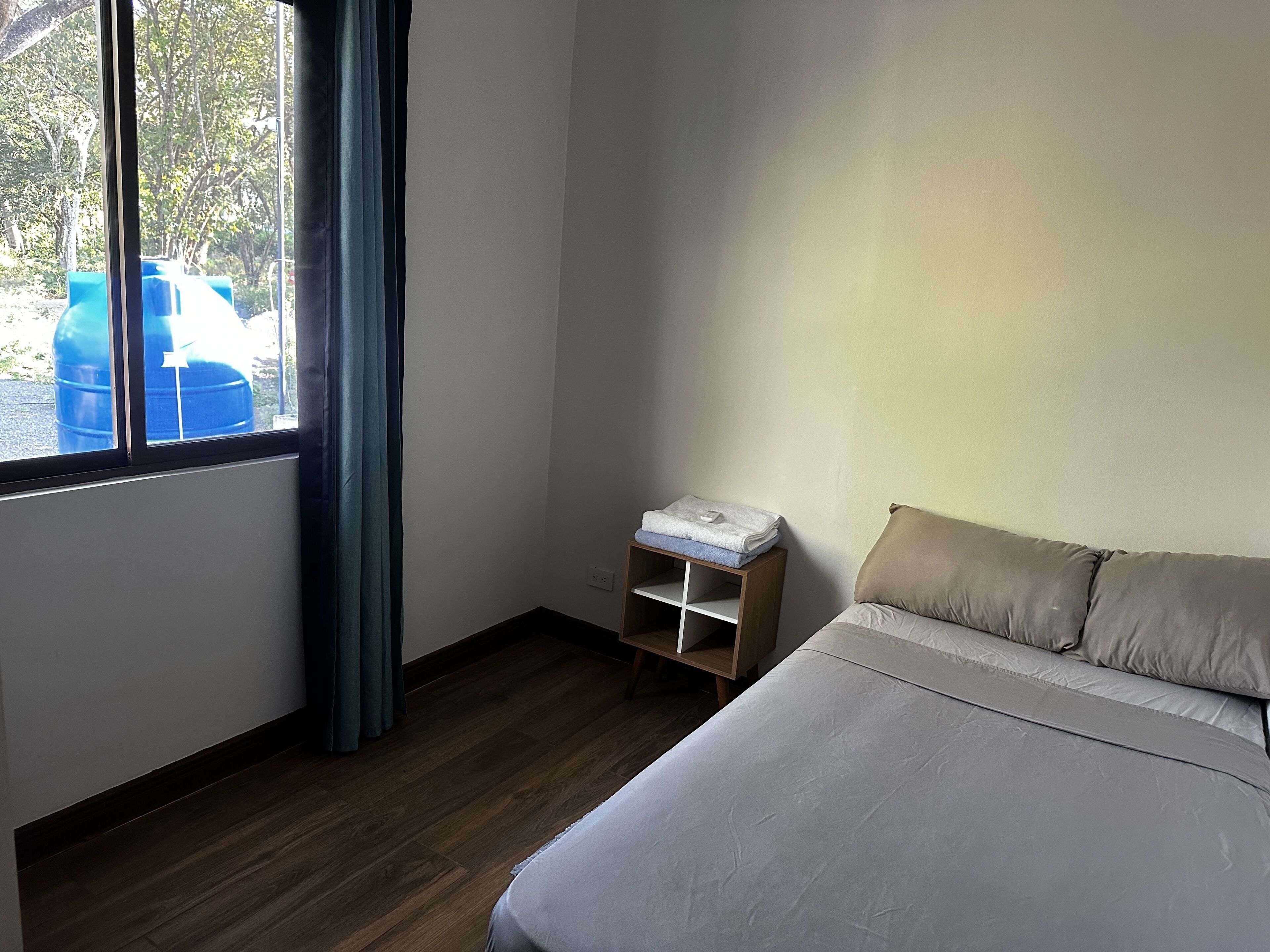 A bedroom with a bed, a nightstand, a window with curtains, and a view of trees outside.