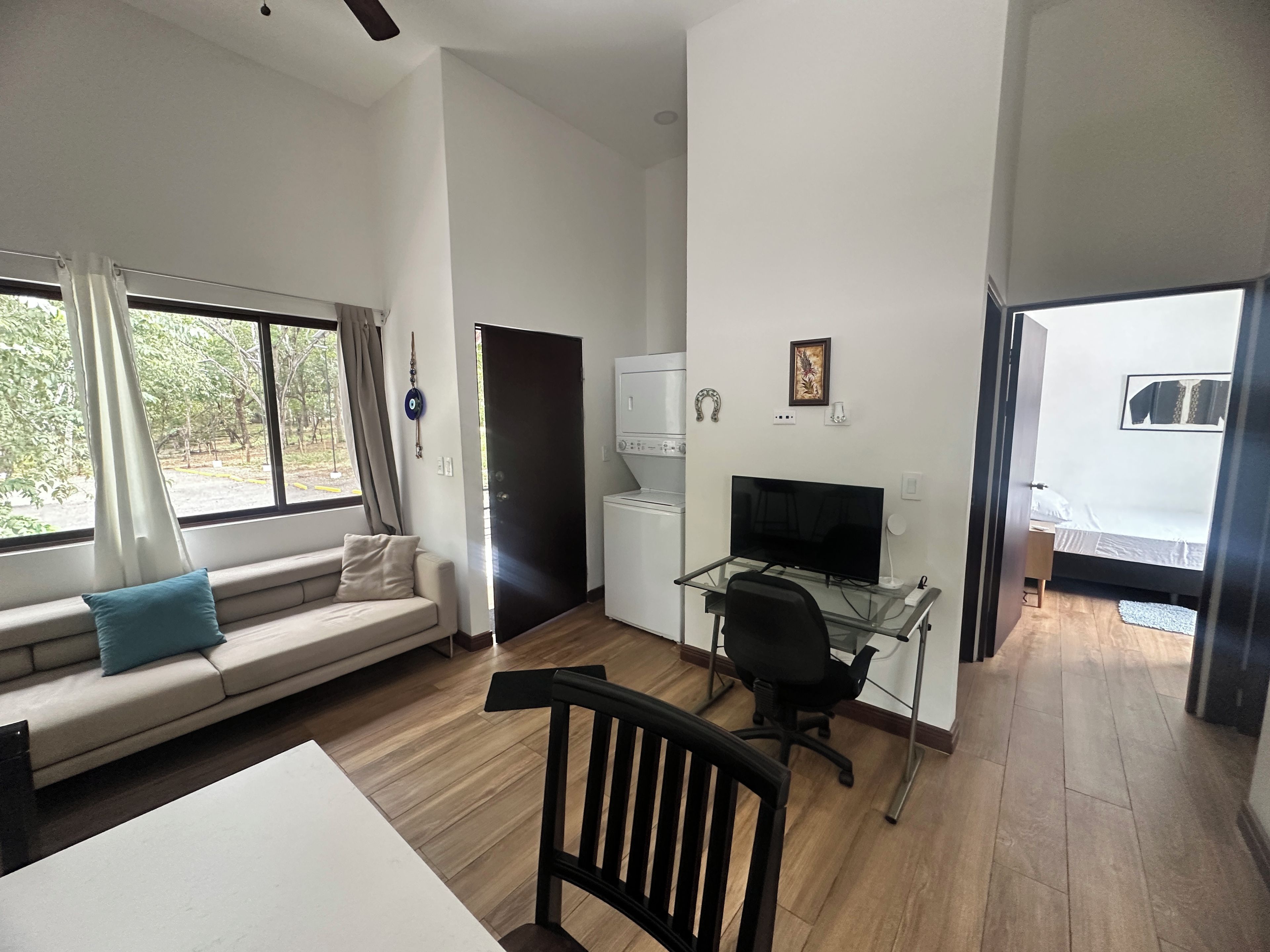 A modern room with a sofa, a desk with a computer, a bed, and a window with curtains.