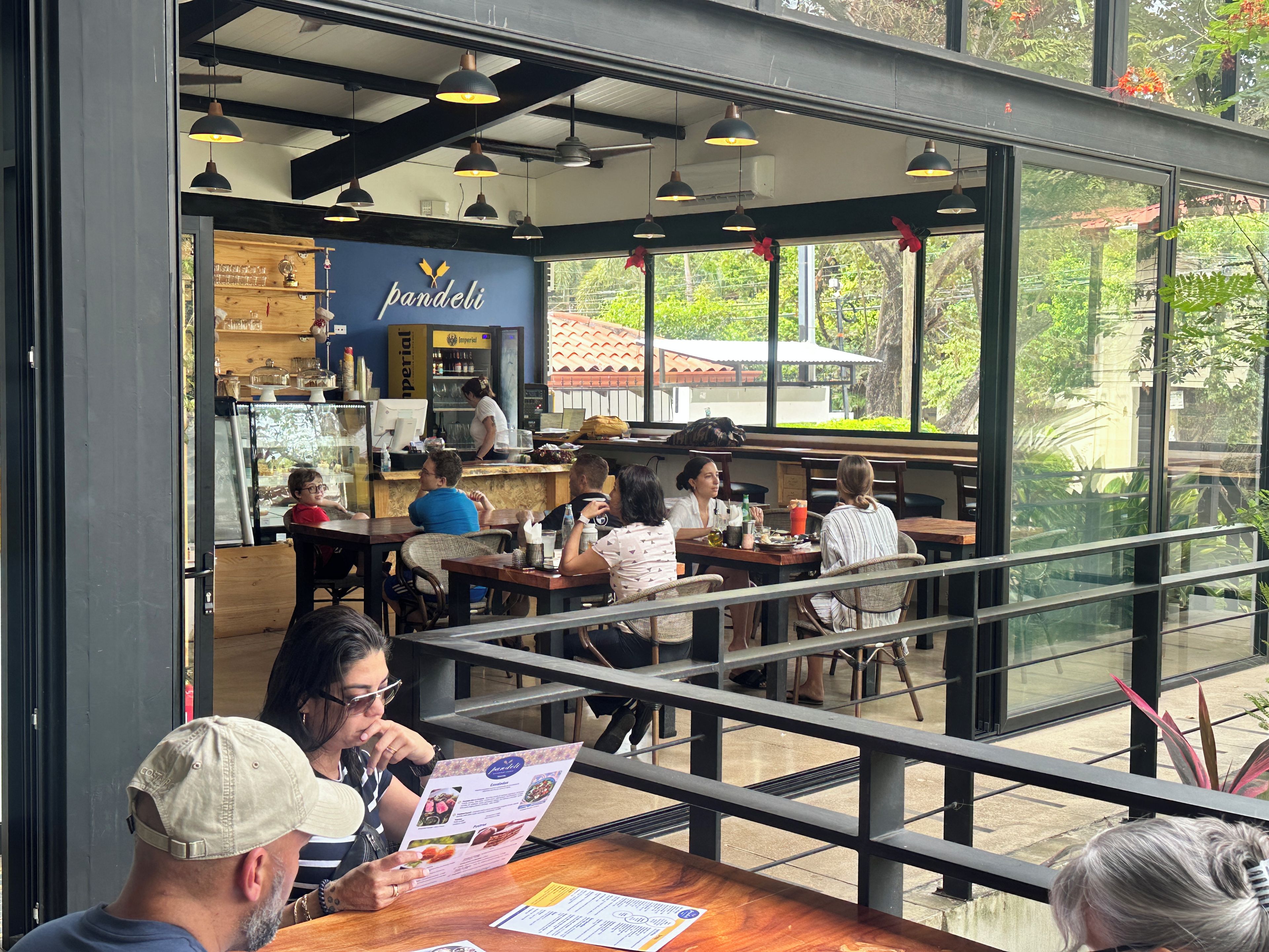 Un espace de restauration intérieur avec des tables et des chaises, un comptoir où se tient un employé, et de grandes fenêtres donnant sur un paysage verdoyant.