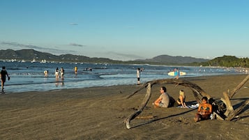 Una playa con gente, una tabla de surf y barcos en el agua.