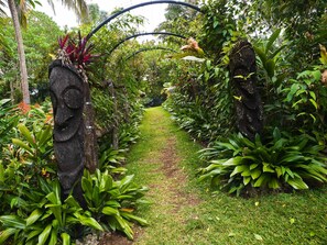 A garden pathway flanked by lush greenery and a stone sculpture. - Eden on the River (Rentapow)