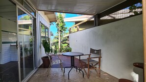 Un pequeño patio al aire libre con mesa y sillas, una planta en maceta y una puerta corrediza de vidrio que da a una habitación con baldosas.