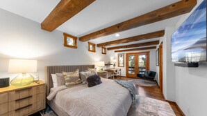A bedroom with a large bed, wooden beams, a desk, and a view of the outdoors. - Highlands Hideaway  By Tahoe Getaways - 4BR, Pet Friendly w Hot Tub (Tahoe City)
